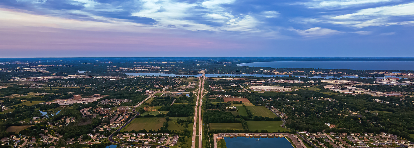 Aerial view of a highway at dusk stretching over a green landscape toward a large lake.